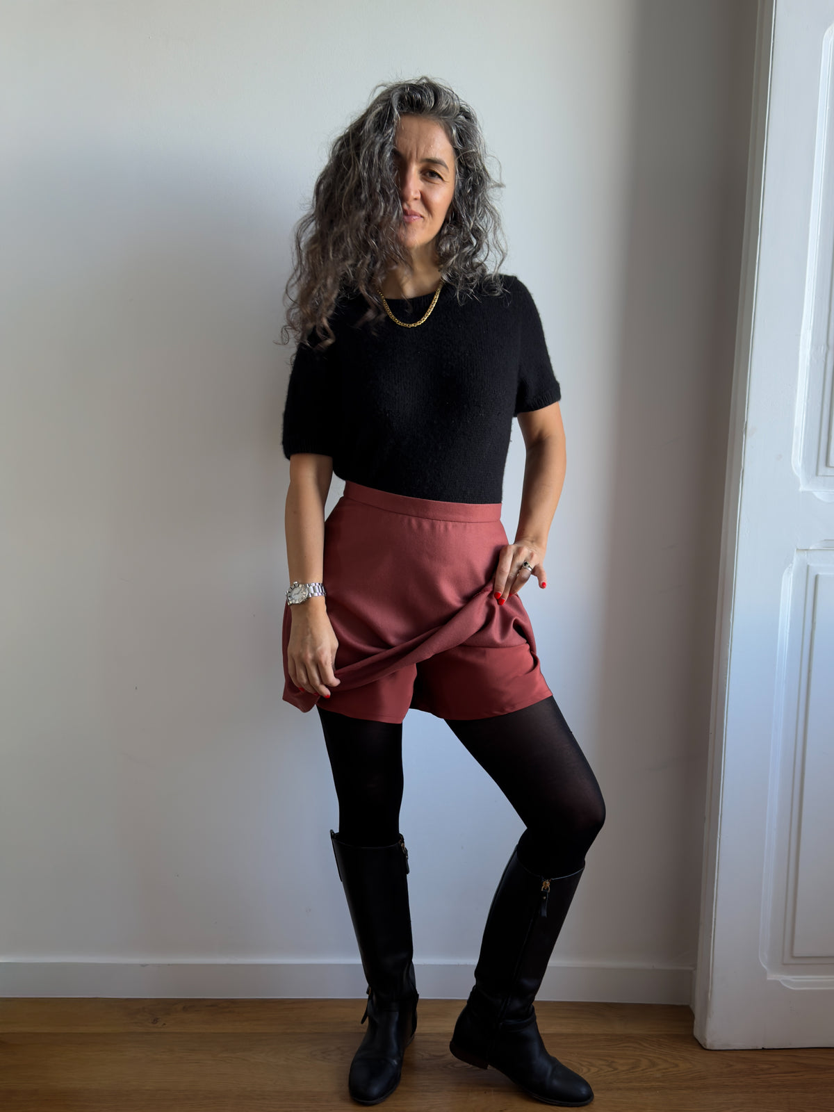 Karlie Skort sewing pattern, view A in the longer length, rust wool skirt lifted over the silk shorts, with tights and boots